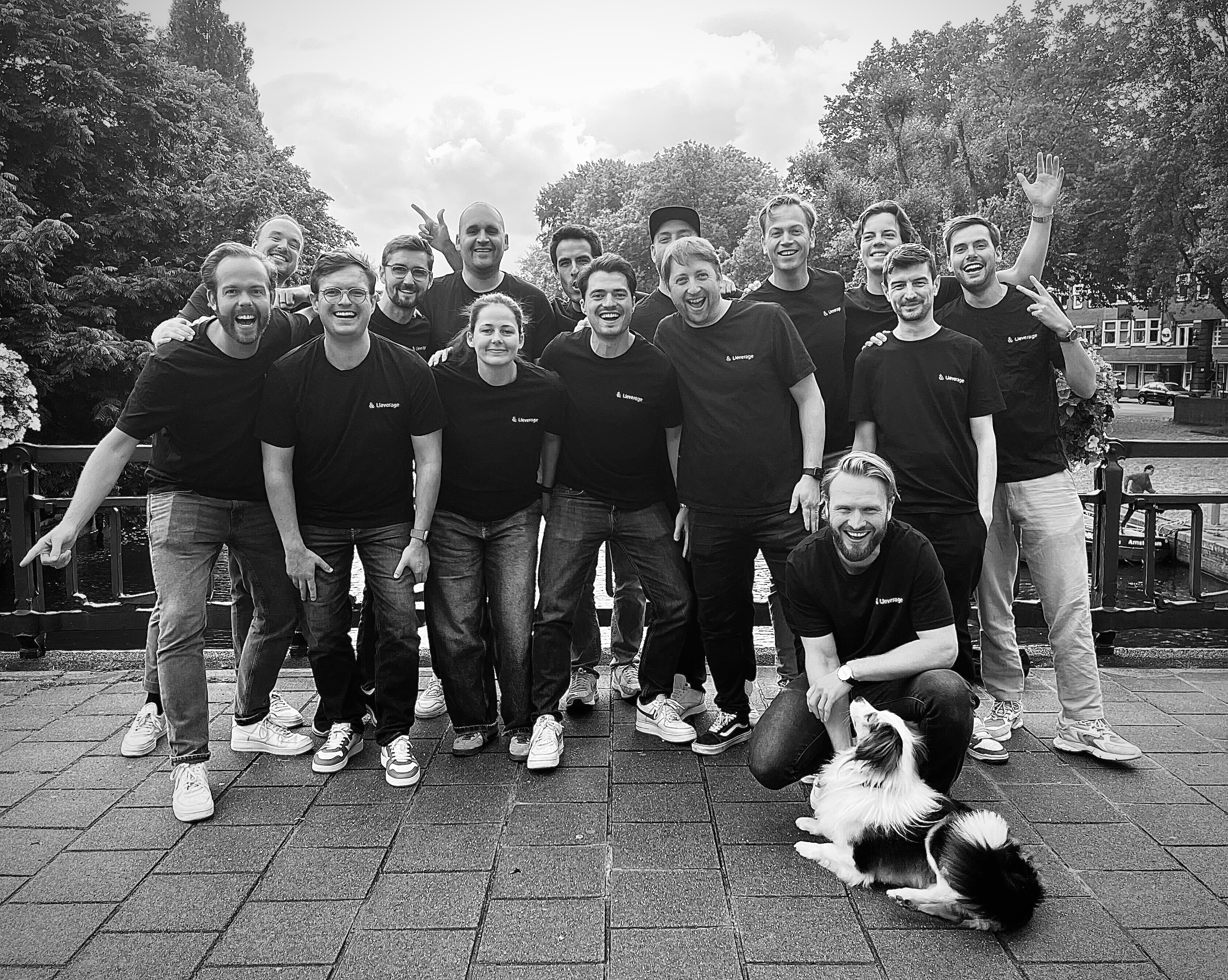 The Lleverage team in branded T-shirts, gathered on an Amsterdam canal bridge with a dog
