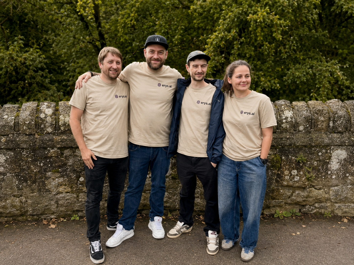 The four person Erys AI team in branded T-shirts, standing against a stone wall